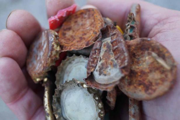 Eine Hand hält eine Sammlung von rostigen Kronkorken und anderen Metallteilen.