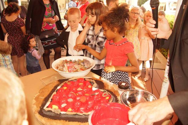 Kinder stehen an einem Tisch mit einer herzförmigen Torte und einer Schüssel mit Süßigkeiten.