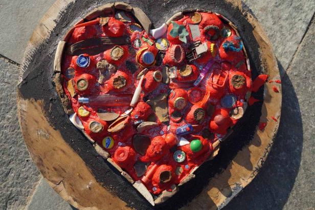 Ein herzförmiges Kunstwerk aus roter Farbe und verschiedenen Fundstücken auf Holz.