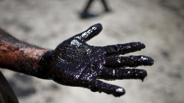 Volunteers carry buckets of oil from an oil slick Eine Hand und ein Unterarm sind mit einer dicken, glänzenden, schwarzen Substanz bedeckt.