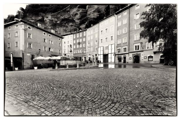 Ein Platz mit Kopfsteinpflaster und einem Brunnen in Salzburg, Österreich.