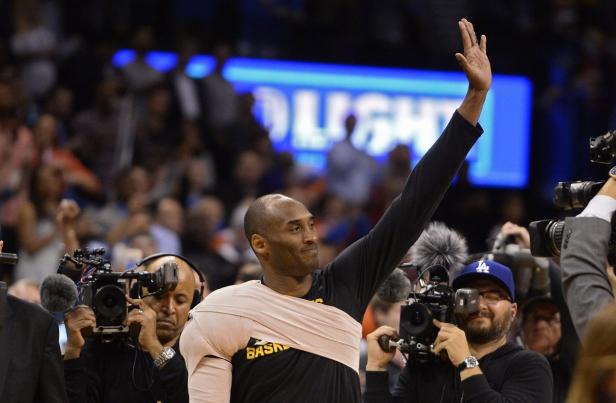 Kobe Bryant winkt mit bandagiertem Arm vor einer Menge Fotografen.