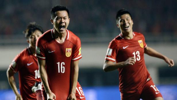 Jubelnde chinesische Fußballspieler in roten Trikots.