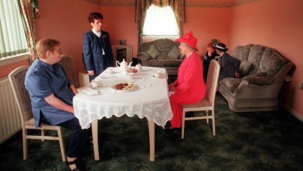 Königin Elisabeth II. sitzt bei einer Teestunde in einem Wohnzimmer.