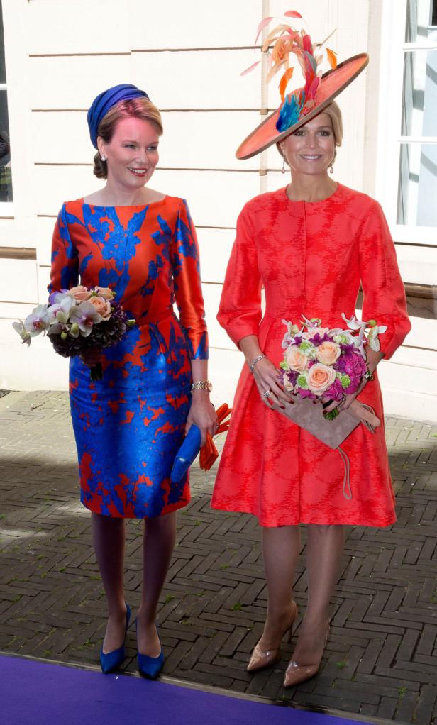 Königin Mathilde und Königin Máxima mit Blumensträußen bei einem formellen Anlass.