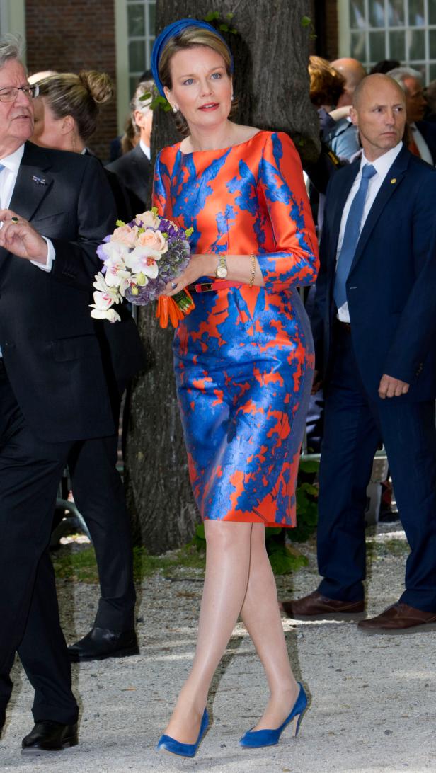 Königin Mathilde von Belgien mit einem Blumenstrauß in einem orange-blauem Kleid.