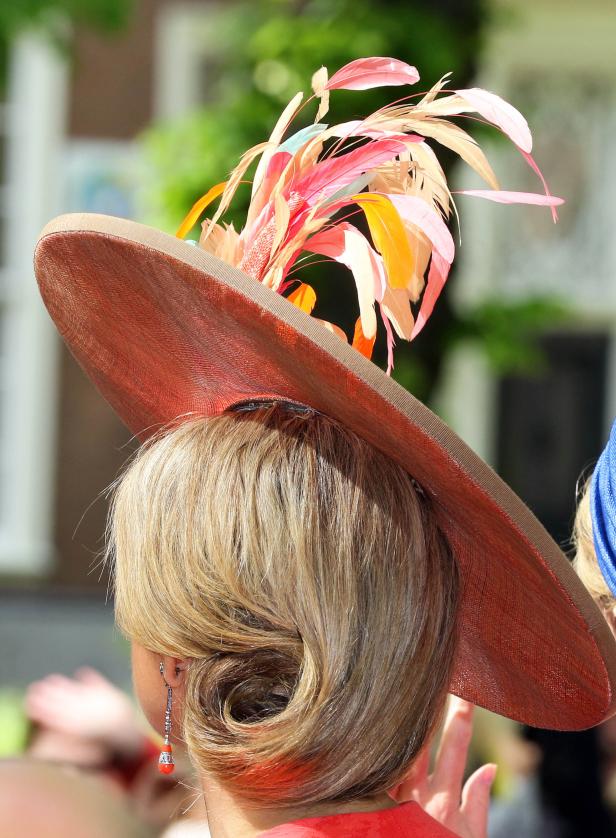 Eine Frau mit blonden Haaren trägt einen auffälligen Hut mit Federn.