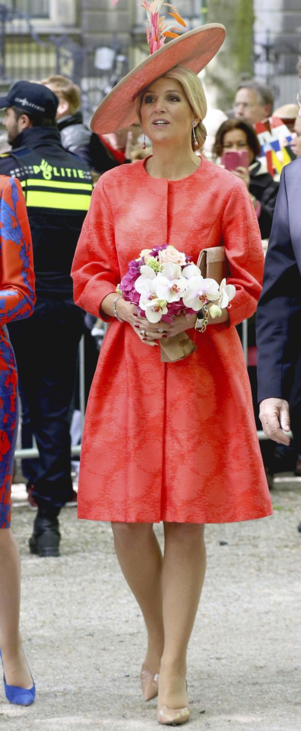 Königin Máxima mit einem orangefarbenen Kleid und einem Blumenstrauß.