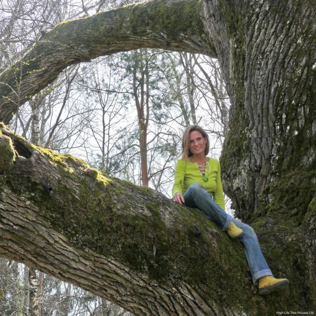 Eine Frau sitzt auf einem moosbewachsenen Ast eines großen Baumes.