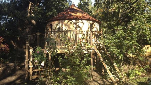 Ein rundes Baumhaus mit einem kegelförmigen Dach inmitten von Bäumen.