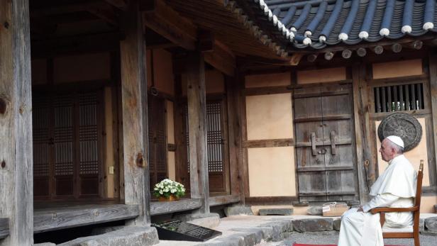Papst Franziskus sitzt vor einem traditionellen koreanischen Haus.