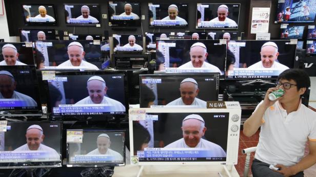 Ein Mann trinkt vor einer Wand von Fernsehern, die Papst Franziskus zeigen.