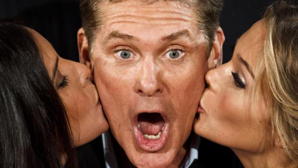 David Hasselhoff wird von zwei Frauen auf die Wange geküsst.