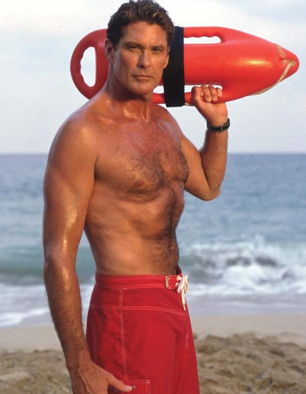 David Hasselhoff in roter Badehose mit Rettungsboje am Strand.