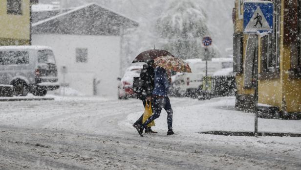 Zwei Personen mit Regenschirmen überqueren eine verschneite Straße.