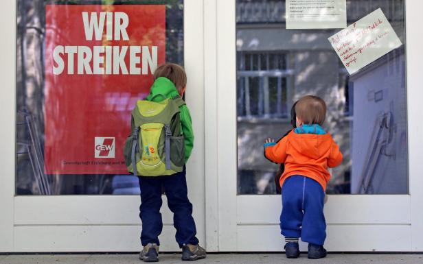 Zwei Kinder stehen vor einer Tür mit dem Aufdruck „Wir Streiken“.