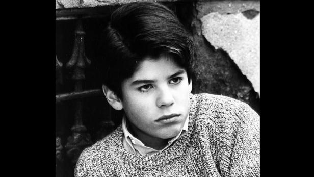 Ein junger Mann mit dunklen Haaren und einem Strickpullover blickt nachdenklich zur Seite.