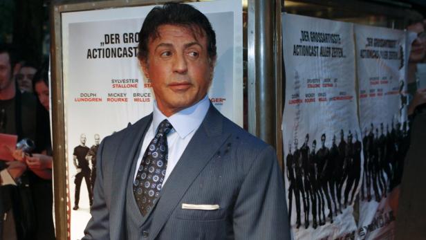 Sylvester Stallone posiert vor einem Poster für „The Expendables“.