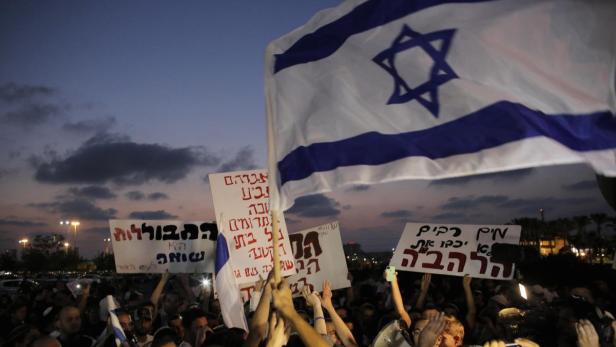 Eine Menschenmenge demonstriert mit israelischen Flaggen und Schildern bei Dämmerung.