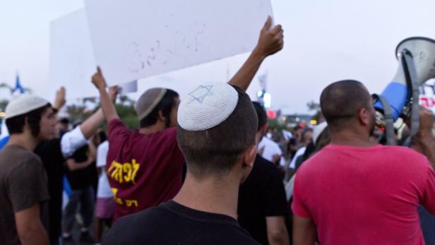 Eine Gruppe von Menschen demonstriert, einige tragen Kippas und halten Schilder hoch.