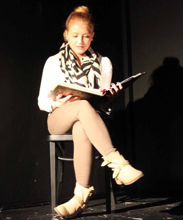 Eine junge Frau sitzt auf einem Stuhl und liest in einem Buch.