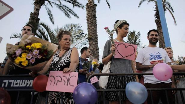 Menschen demonstrieren mit Blumen, Ballons und Schildern vor einer Absperrung.