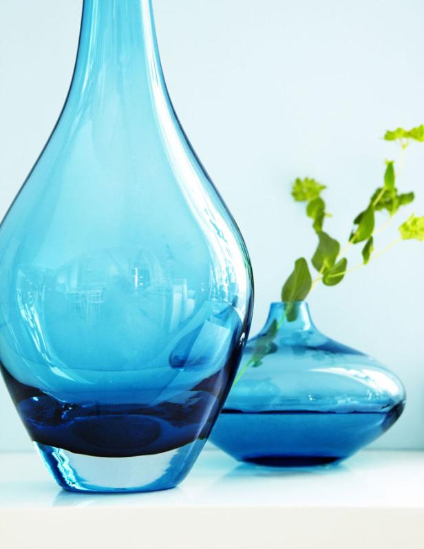 Zwei blaue Glasvasen stehen auf einer weißen Oberfläche, eine davon mit einer grünen Pflanze.