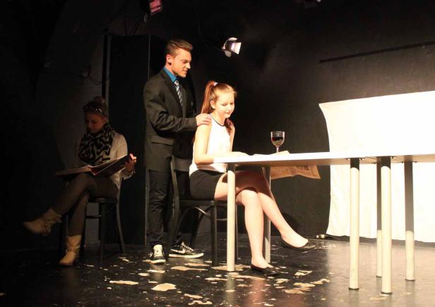 Auf einer Bühne sitzen zwei Frauen und ein Mann an einem Tisch.