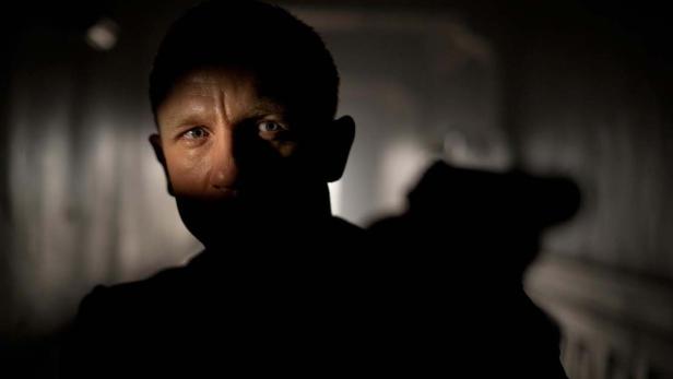 Ein Mann steht im Dunkeln, nur sein Gesicht ist teilweise beleuchtet.