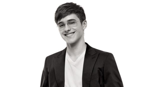 Ein junger Mann mit Brille lächelt in einem schwarzen Sakko.