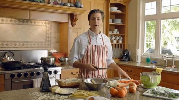 Ein Mann mit Schürze steht in einer Küche und bereitet Zutaten für Lasagne vor.