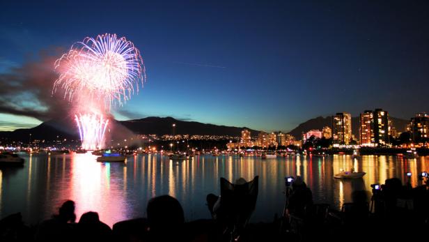 Feuerwerk erhellt den Nachthimmel über einer Stadt am Wasser.