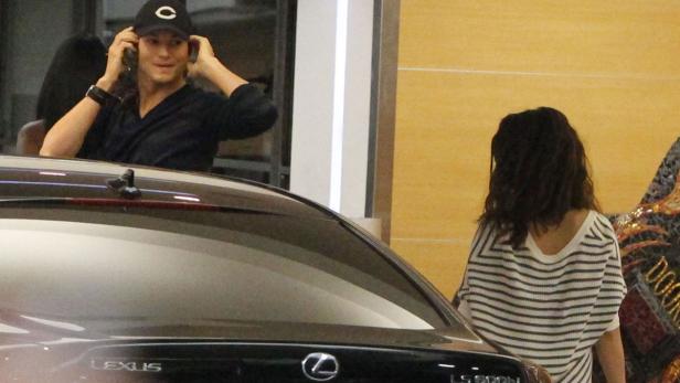 Ashton Kutcher steigt in seinen Lexus, während eine Frau daneben steht.