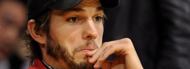 Ashton Kutcher mit Bart und Baseballkappe, die Hand ans Kinn gelegt.