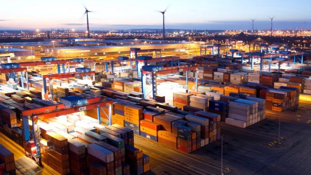 Blick auf einen Containerhafen bei Nacht mit Windrädern im Hintergrund.