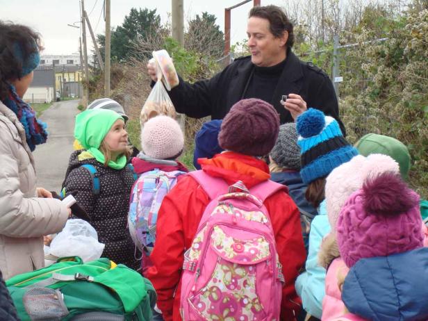 Ein Mann teilt Kekse an eine Gruppe von Kindern im Freien aus.