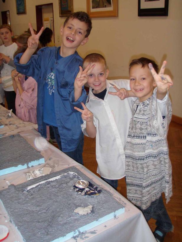 Drei Jungen posieren mit Friedenszeichen vor einem Tisch mit Bastelarbeiten.