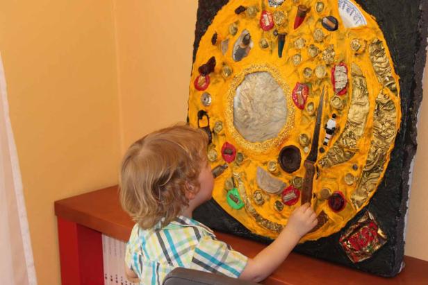 Ein Kind betrachtet ein gelbes Kunstwerk mit verschiedenen Objekten.