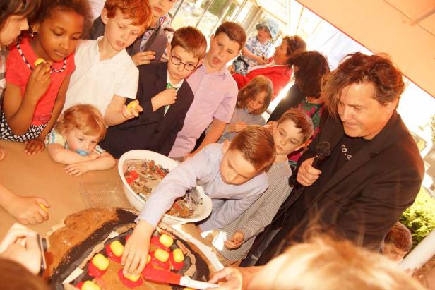 Eine Gruppe von Kindern und ein Mann gestalten gemeinsam eine große Torte.