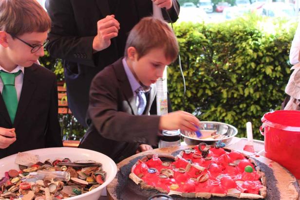Zwei Jungen in Anzügen basteln an einem Kunstprojekt mit roter Farbe und verschiedenen Objekten.
