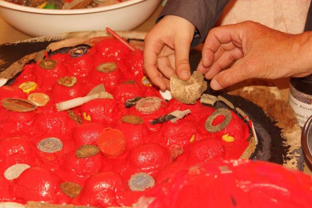 Zwei Personen gestalten ein rotes Objekt mit verschiedenen Materialien.