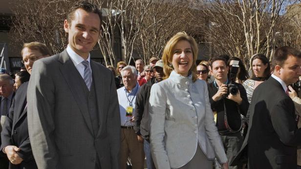 Ein Mann im Anzug und eine Frau in einer hellen Jacke lächeln in die Kamera, umgeben von Menschen.