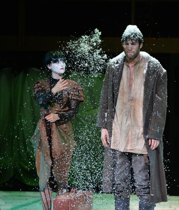 Zwei Schauspieler in Kostümen stehen in einem Schneegestöber auf der Bühne.