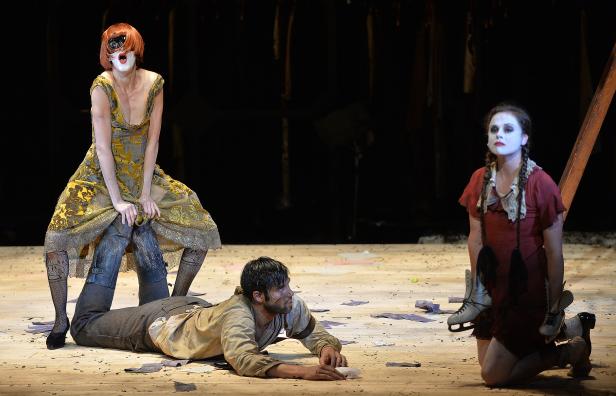 Szene einer Theateraufführung mit drei Schauspielern in Kostümen und Make-up.