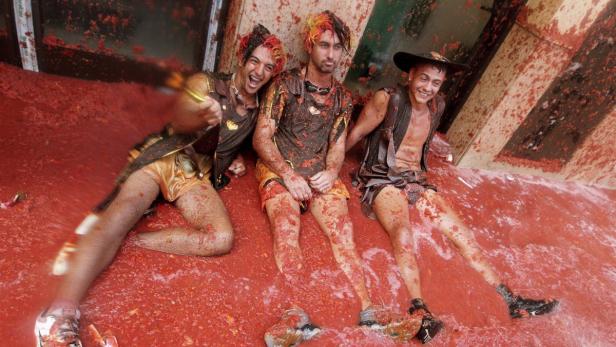 Drei Männer liegen während der Tomatina-Schlacht in Buñol, Spanien, in einer dicken Schicht Tomaten.