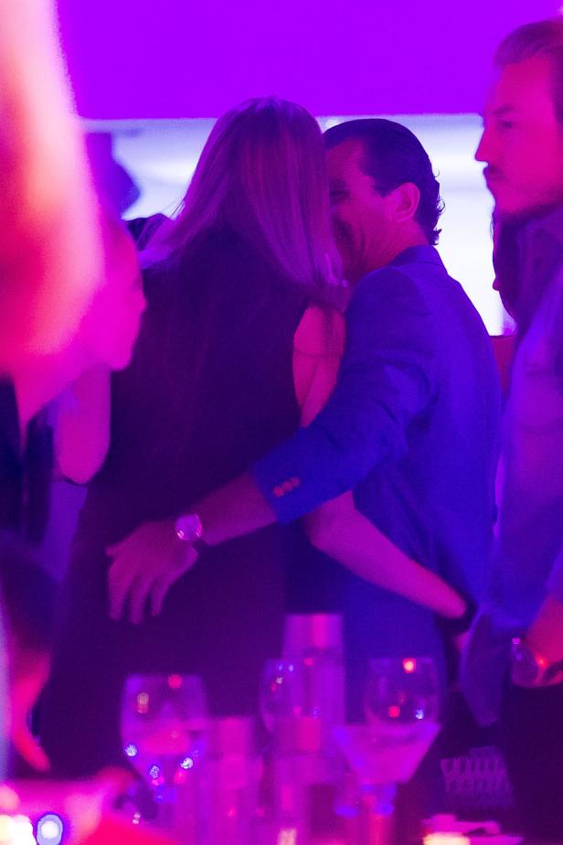 Ein Mann im blauen Sakko umarmt eine Frau auf einer Party mit violetter Beleuchtung.