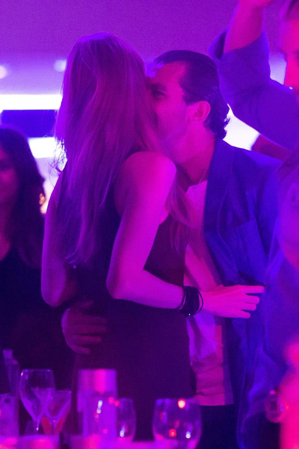 Ein Paar umarmt sich und küsst sich in einem Club mit violetter Beleuchtung.