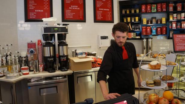 Ein Mann in einem Café steht hinter der Theke mit Kaffee und Gebäck.