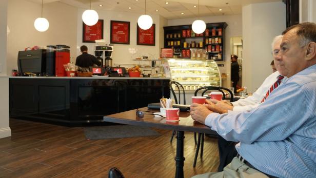 Zwei Männer sitzen in einem Café an einem Tisch und trinken Kaffee.