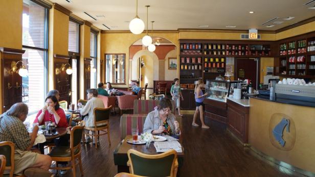 In einem Café sitzen mehrere Personen an Tischen und genießen Speisen und Getränke.
